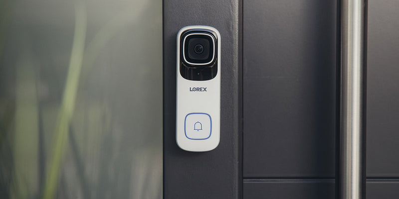 The Lorex 4K Wi-Fi Video Doorbell, a sleek white smart doorbell with a camera and bell icon button, is mounted on a modern doorframe.